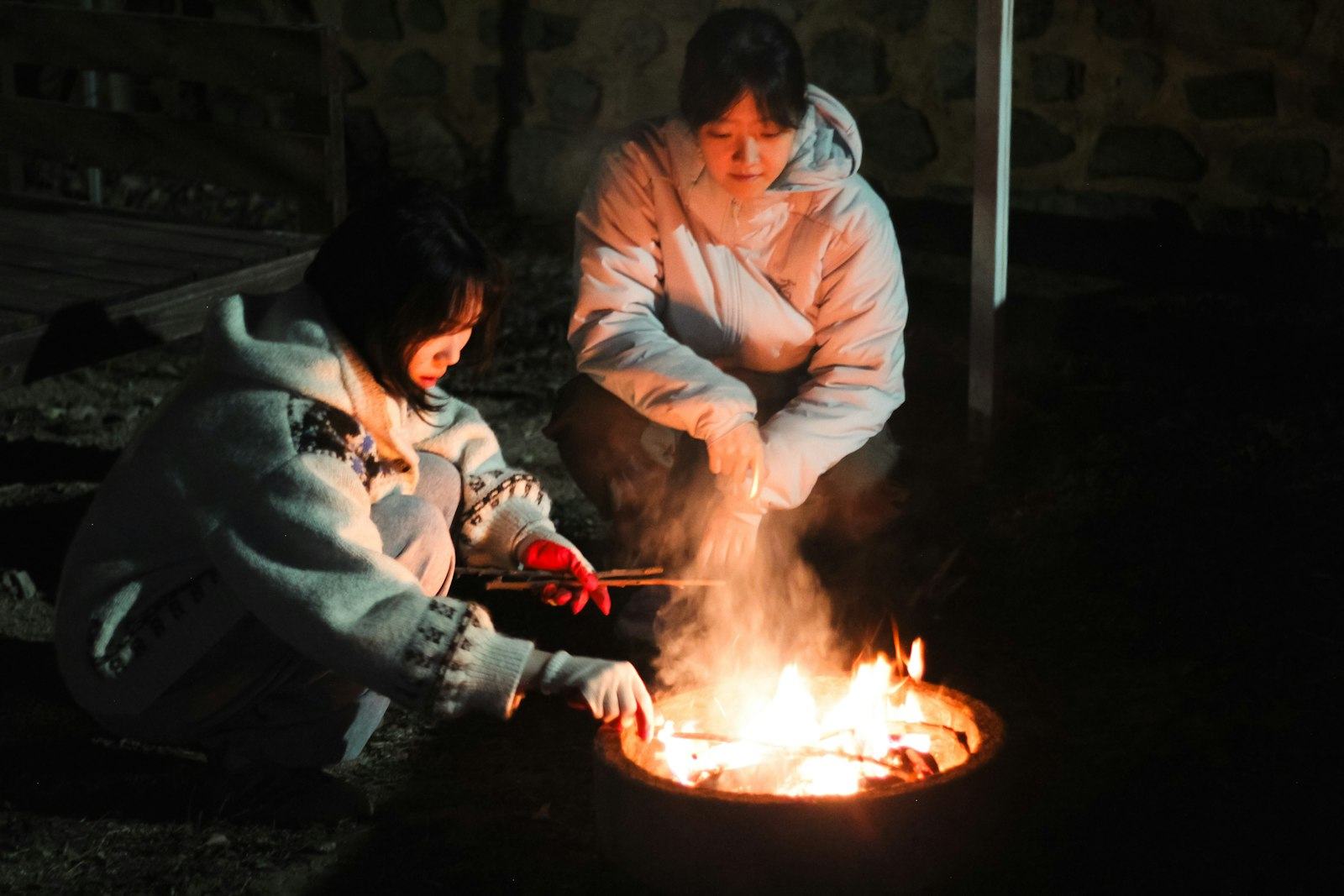 Two people tending a fire at night
